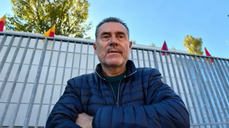 Un uomo in primo piano davanti a una recinzione con bandiere sullo sfondo