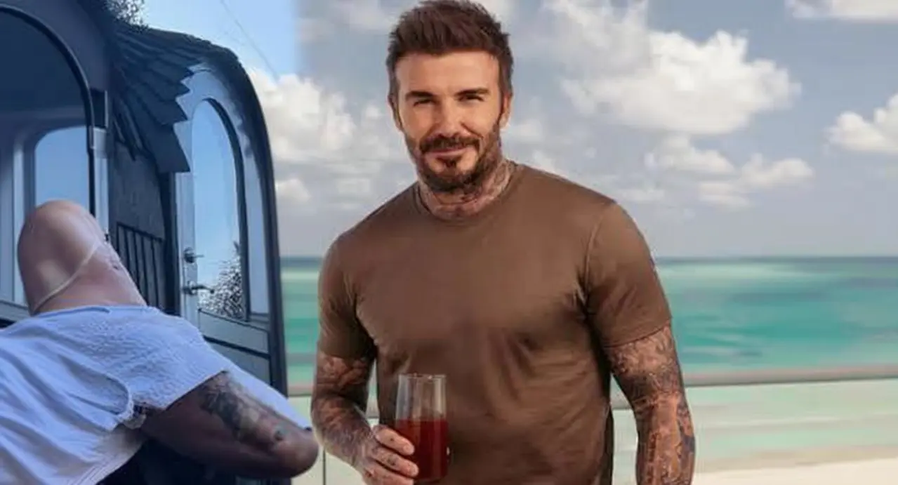 Una persona con tatuaggi tiene un bicchiere con bevanda rossa davanti al mare