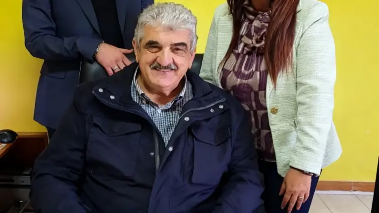 Tre persone posano sorridenti in un ambiente interno con parete gialla