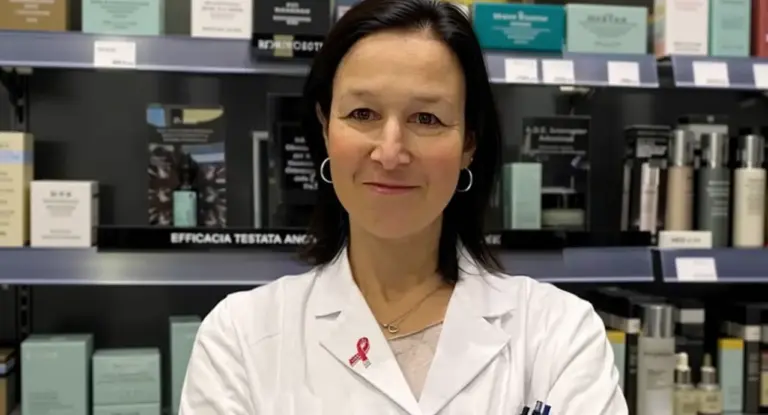 Una persona in camice bianco in una farmacia, circondata da prodotti sugli scaffali