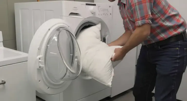 Una persona inserisce un cuscino bianco in una lavatrice a carica frontale