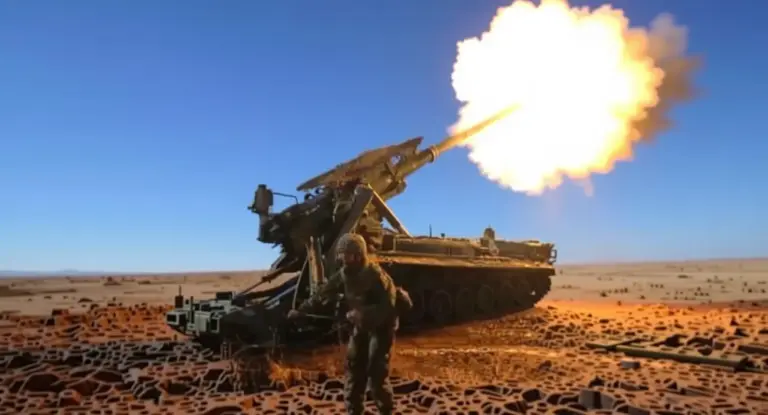 Un soldato vicino a un obice semovente che spara in un paesaggio desertico