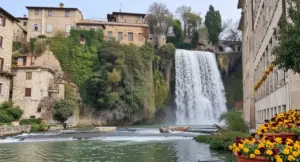 Cascata scenografica nel centro storico di un borgo italiano con edifici in pietra e vegetazione rigogliosa