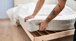 Persona che solleva un materasso da una struttura in legno in una camera da letto