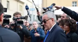 Un uomo in giacca e cravatta circondato da giornalisti e telecamere fuori dal tribunale