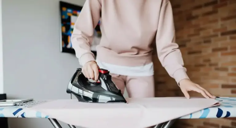Persona che stira a casa con un ferro da stiro moderno su un asse da stiro