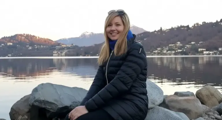 Una persona seduta su rocce vicino a un lago con colline sullo sfondo