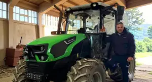 Persona accanto a un trattore verde all'interno di un capannone agricolo